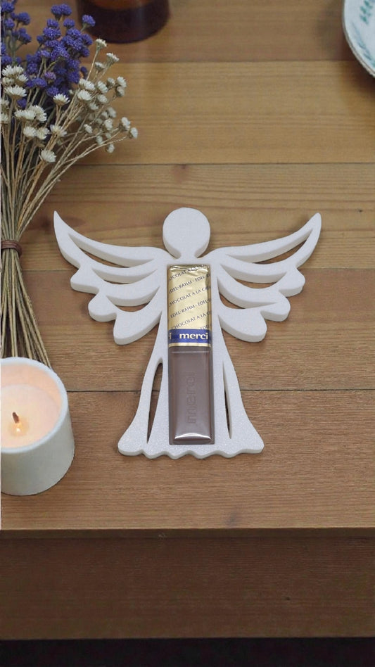 Nahaufnahme der 3D-gedruckten Engel-Halterung für Merci Schokolade, platziert auf einem Holztisch mit Kerzen und Blumen.