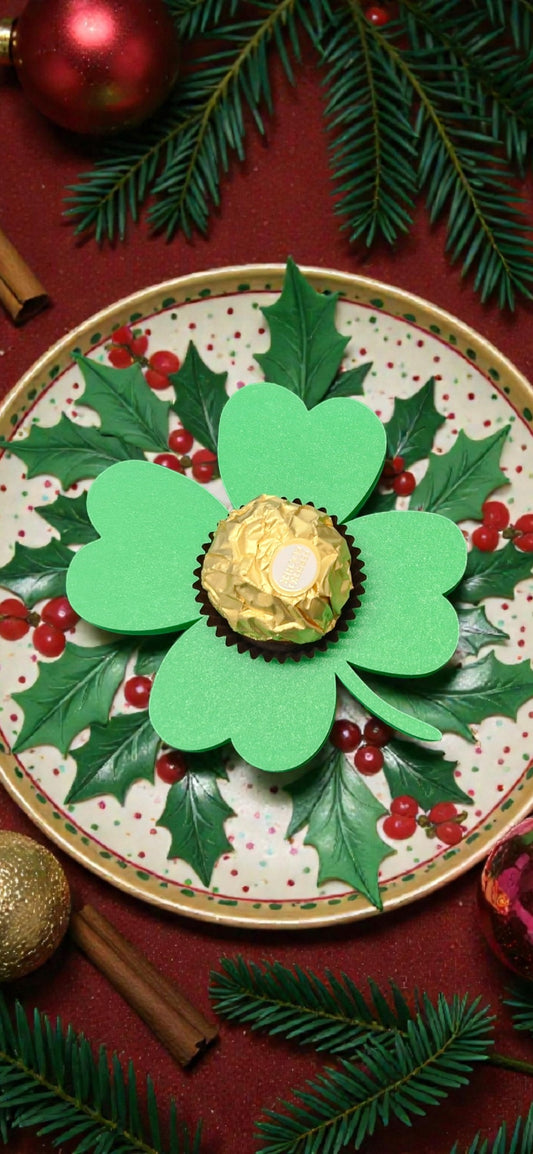 Festliche Tischdekoration von BTE Deutschland mit einem grünen Glücksklee-Halter für Ferrero Rocher auf einem weihnachtlichen Teller mit Tannenzweigen.